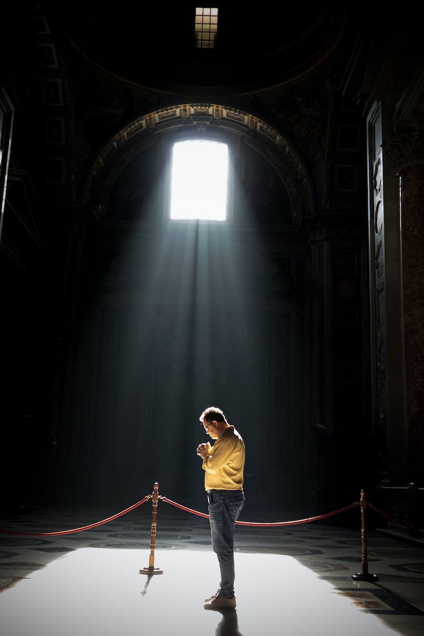 unrecognizable man praying in church in sunlight